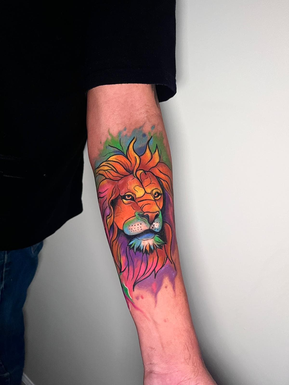 Vibrant watercolor color lion head tattoo on a forearm with a rainbow mane