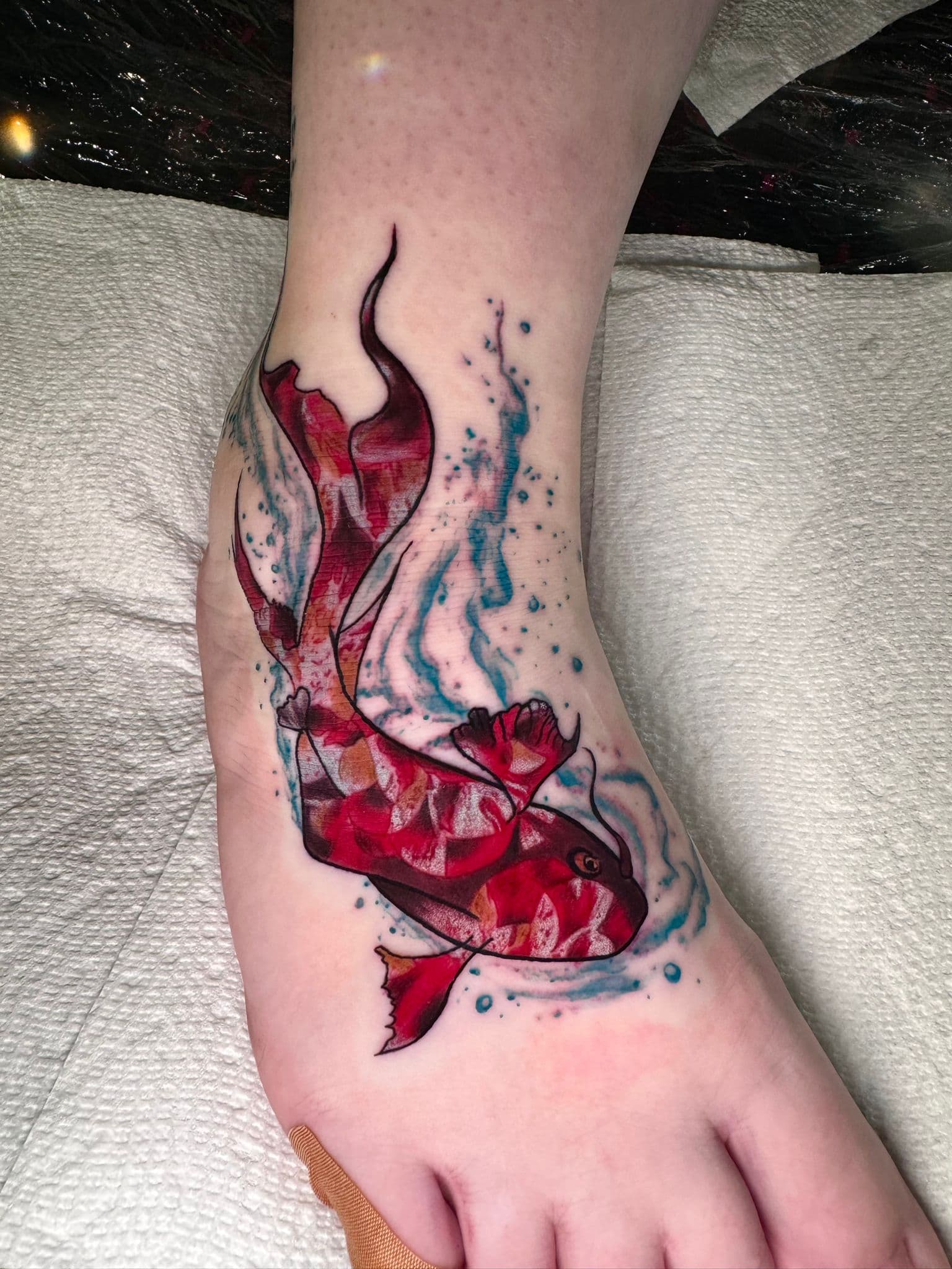 New-school red koi fish tattoo on a foot with blue watercolor splashes