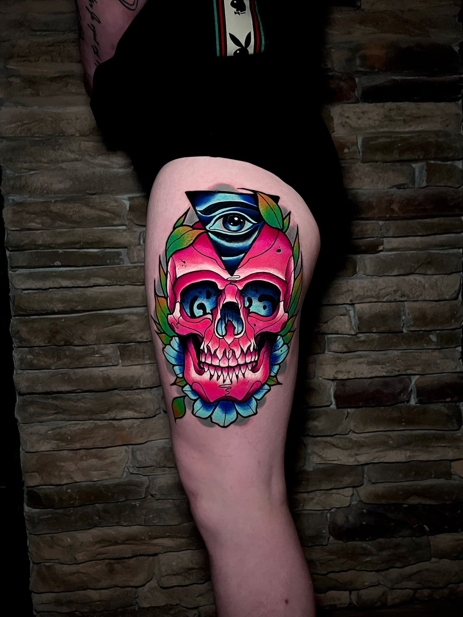 Neo-traditional color skull tattoo on a thigh with an all-seeing eye and bold flowers