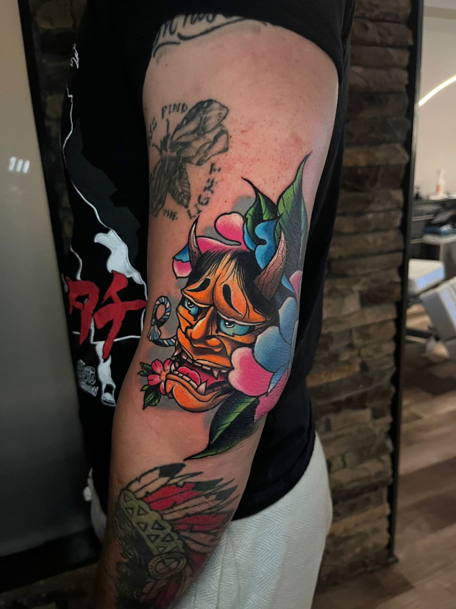Neo-traditional Hannya demon mask tattoo on an upper arm with bold clouds and a flower