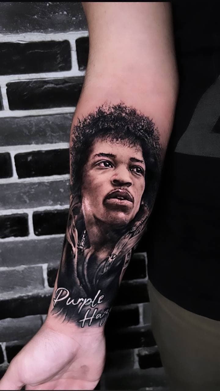 Black-and-grey realism portrait tattoo of Jimi Hendrix on a forearm with Purple Haze lettering