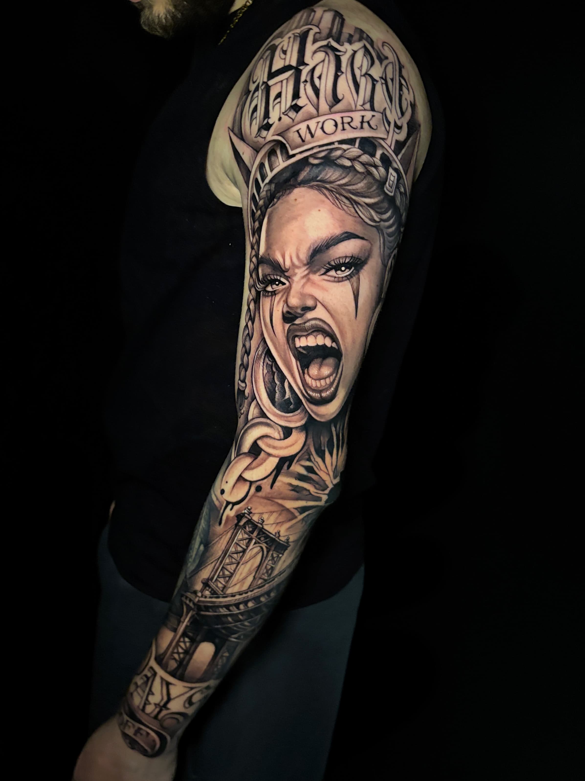 Black-and-grey Chicano-style sleeve tattoo of a screaming woman with Hard Work lettering and a bridge